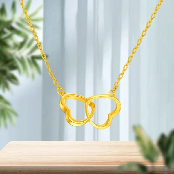 Golden Interlocking Heart Necklace on wooden surface with green plant background