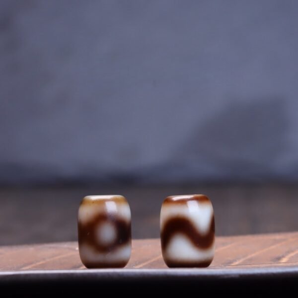 Natural Tibetan dzi bead, tiger tooth three-eye dzi, barrel-shaped spacer bead, yellowish-brown dzi bead, jewelry making supplies, Buddhist prayer beads, authentic weathering marks, Tibetan cultural artifact, spiritual symbol bead, handmade dzi bead, vintage-inspired jewelry, earthy tone spacer, mystical patterns, top bead for necklaces, bracelet accent bead, cultural craft material, protection symbol bead, wisdom dzi design, artisan jewelry component, collectible spiritual bead.