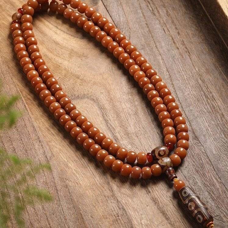 108-bead Buddhist mala, honey-colored prayer beads, natural seed necklace, meditation necklace, spiritual protection pendant, eye motif mala, handmade Buddhist jewelry, mindfulness accessory, Zen lifestyle gift, eco-friendly spiritual tool, unisex mala necklace, prayer beads for meditation, traditional mala design, earthy tone jewelry, calming energy beads, Buddhist ritual accessory, durable natural beads, minimalist spiritual wear, gift for yoga practitioners, authentic mala necklace.