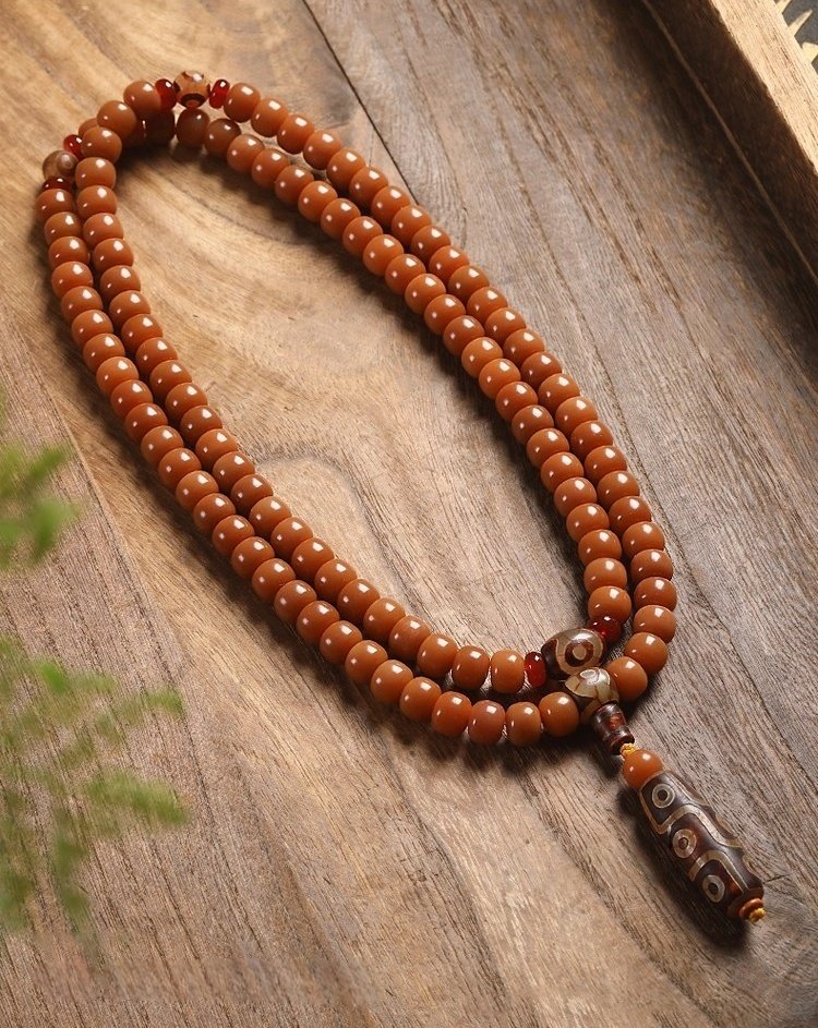 108-bead Buddhist mala, honey-colored prayer beads, natural seed necklace, meditation necklace, spiritual protection pendant, eye motif mala, handmade Buddhist jewelry, mindfulness accessory, Zen lifestyle gift, eco-friendly spiritual tool, unisex mala necklace, prayer beads for meditation, traditional mala design, earthy tone jewelry, calming energy beads, Buddhist ritual accessory, durable natural beads, minimalist spiritual wear, gift for yoga practitioners, authentic mala necklace.