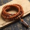 108-bead Buddhist mala, honey-colored prayer beads, natural seed necklace, meditation necklace, spiritual protection pendant, eye motif mala, handmade Buddhist jewelry, mindfulness accessory, Zen lifestyle gift, eco-friendly spiritual tool, unisex mala necklace, prayer beads for meditation, traditional mala design, earthy tone jewelry, calming energy beads, Buddhist ritual accessory, durable natural beads, minimalist spiritual wear, gift for yoga practitioners, authentic mala necklace.
