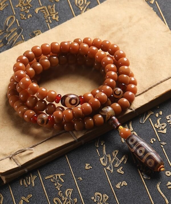108-bead Buddhist mala, honey-colored prayer beads, natural seed necklace, meditation necklace, spiritual protection pendant, eye motif mala, handmade Buddhist jewelry, mindfulness accessory, Zen lifestyle gift, eco-friendly spiritual tool, unisex mala necklace, prayer beads for meditation, traditional mala design, earthy tone jewelry, calming energy beads, Buddhist ritual accessory, durable natural beads, minimalist spiritual wear, gift for yoga practitioners, authentic mala necklace.