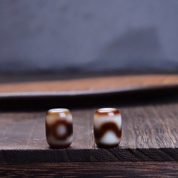Natural Tibetan dzi bead, tiger tooth three-eye dzi, barrel-shaped spacer bead, yellowish-brown dzi bead, jewelry making supplies, Buddhist prayer beads, authentic weathering marks, Tibetan cultural artifact, spiritual symbol bead, handmade dzi bead, vintage-inspired jewelry, earthy tone spacer, mystical patterns, top bead for necklaces, bracelet accent bead, cultural craft material, protection symbol bead, wisdom dzi design, artisan jewelry component, collectible spiritual bead.