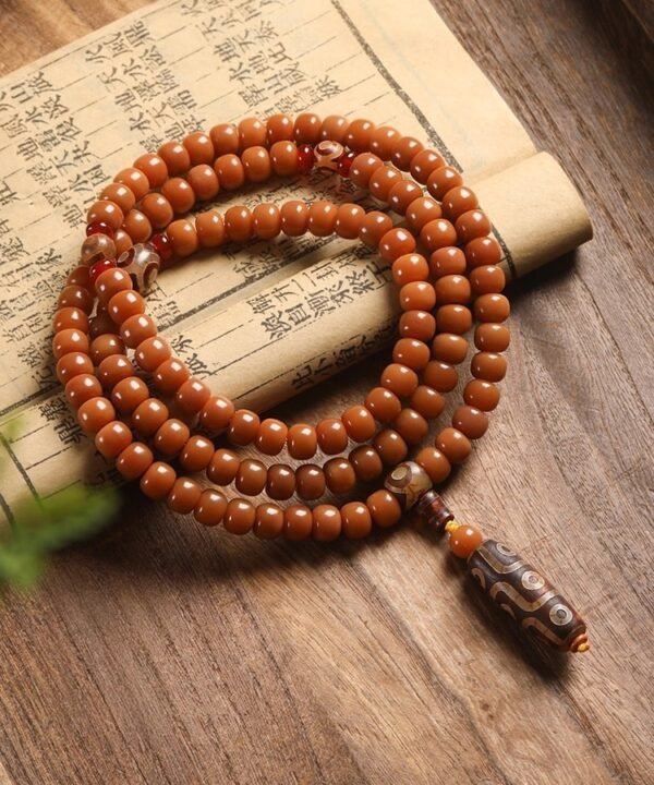 108-bead Buddhist mala, honey-colored prayer beads, natural seed necklace, meditation necklace, spiritual protection pendant, eye motif mala, handmade Buddhist jewelry, mindfulness accessory, Zen lifestyle gift, eco-friendly spiritual tool, unisex mala necklace, prayer beads for meditation, traditional mala design, earthy tone jewelry, calming energy beads, Buddhist ritual accessory, durable natural beads, minimalist spiritual wear, gift for yoga practitioners, authentic mala necklace.
