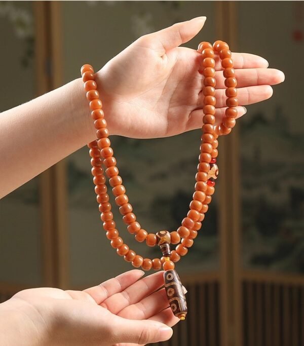 108-bead Buddhist mala, honey-colored prayer beads, natural seed necklace, meditation necklace, spiritual protection pendant, eye motif mala, handmade Buddhist jewelry, mindfulness accessory, Zen lifestyle gift, eco-friendly spiritual tool, unisex mala necklace, prayer beads for meditation, traditional mala design, earthy tone jewelry, calming energy beads, Buddhist ritual accessory, durable natural beads, minimalist spiritual wear, gift for yoga practitioners, authentic mala necklace.